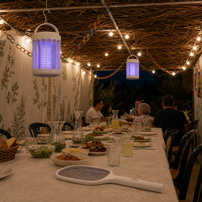 ערכת הסוכה של BuzzOff בסוכה משפחתית מלאה: שתי מנורות UV זוהרות תלויות מהסכך, המחבט החשמלי על שולחן החג, והמשפחה סביב השולחן